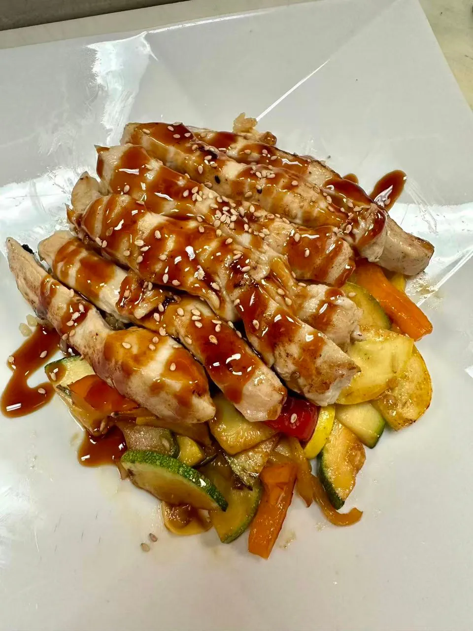 Chicken strips with teriyaki sauce and sesame seeds over stir-fried vegetables