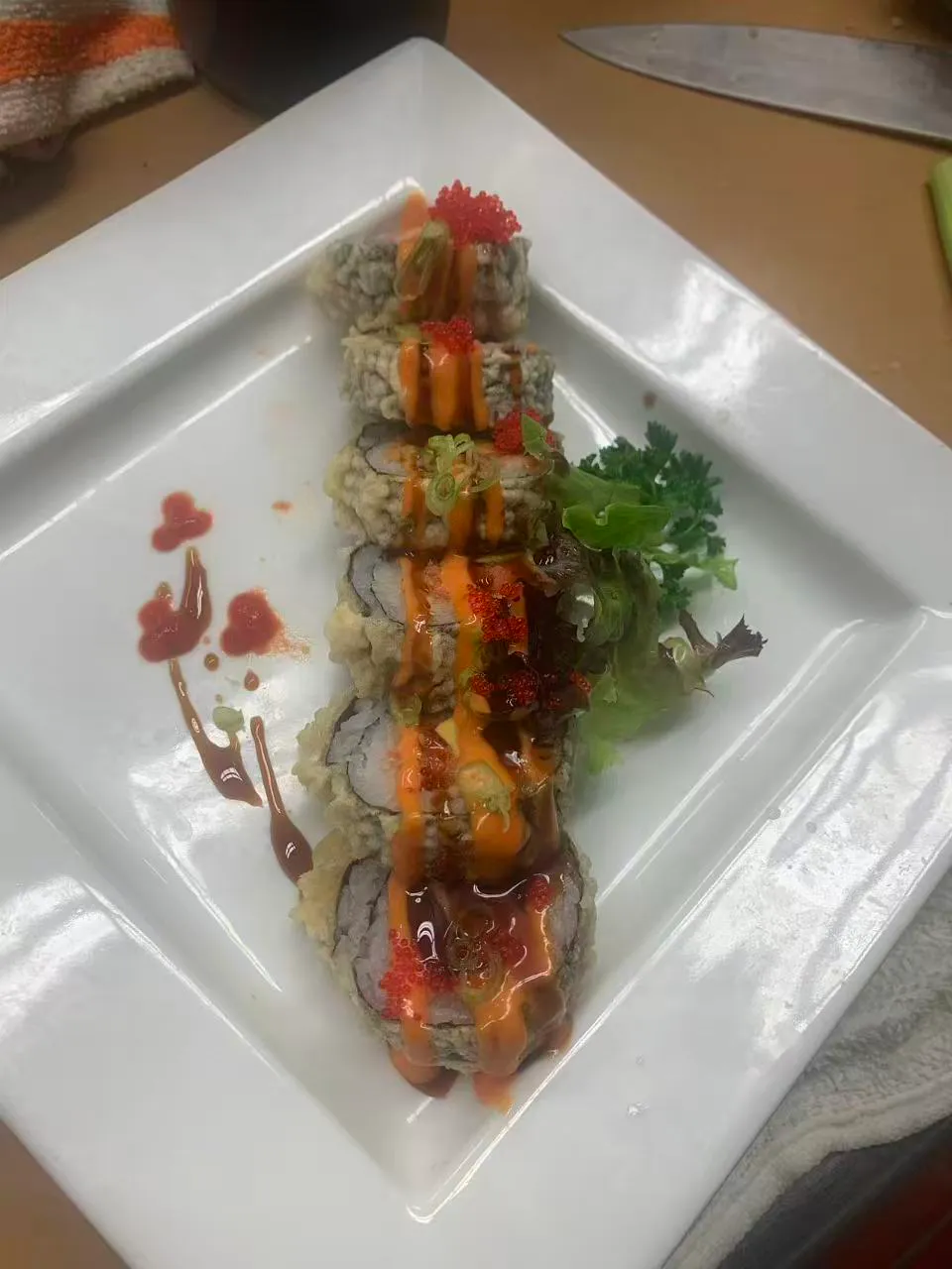 Fried sushi rolls drizzled with spicy mayo and tobiko on a white plate